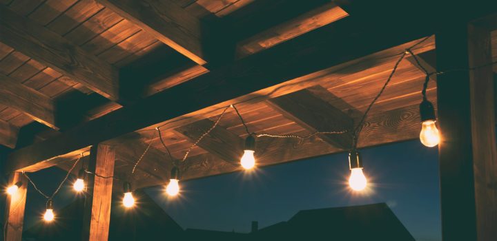 A cozy outdoor patio illuminated by string lights installed under a wooden beam structure, enhancing the home's exterior ambiance.