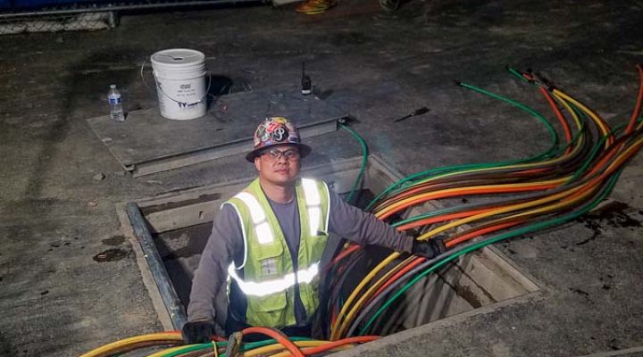An electrician working on underground electrical conduits at night, showcasing the critical infrastructure work involved in electrical installations.