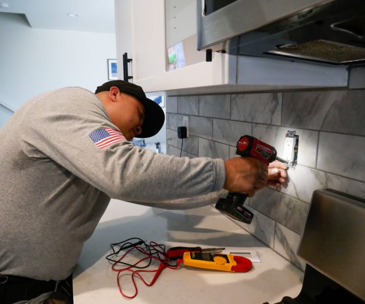 An electrician works on installing a new outlet in a kitchen, highlighting his detailed approach to residential electrical services.