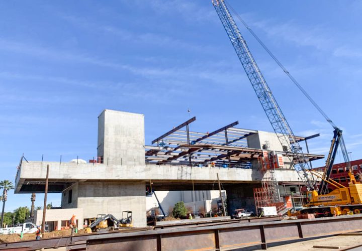 A construction site for a large commercial building with a crane lifting steel beams, showcasing the scale and complexity of modern construction.