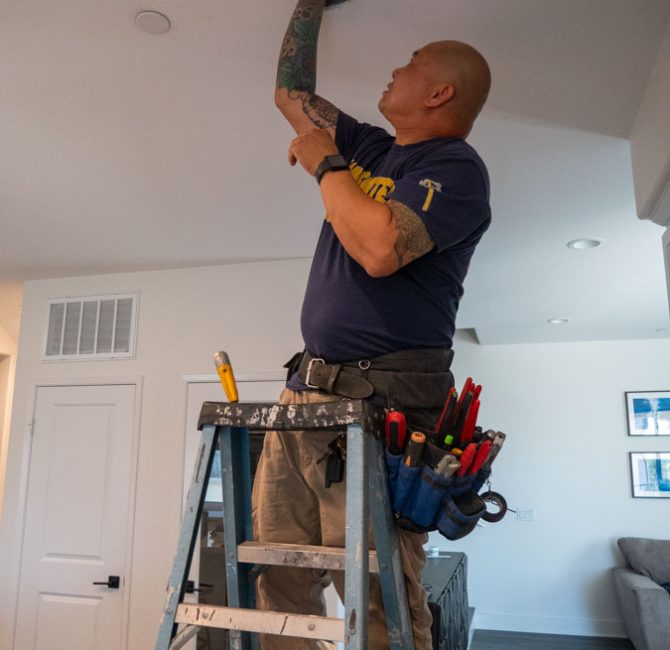 Professional electrician securely attaching a new ceiling light, showcasing skilled electrical installations in a modern living space.